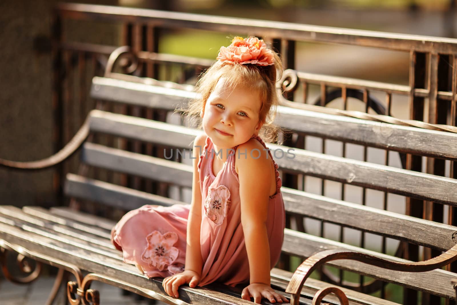 Portrait of a smiling pretty little girl sitting on a park bench