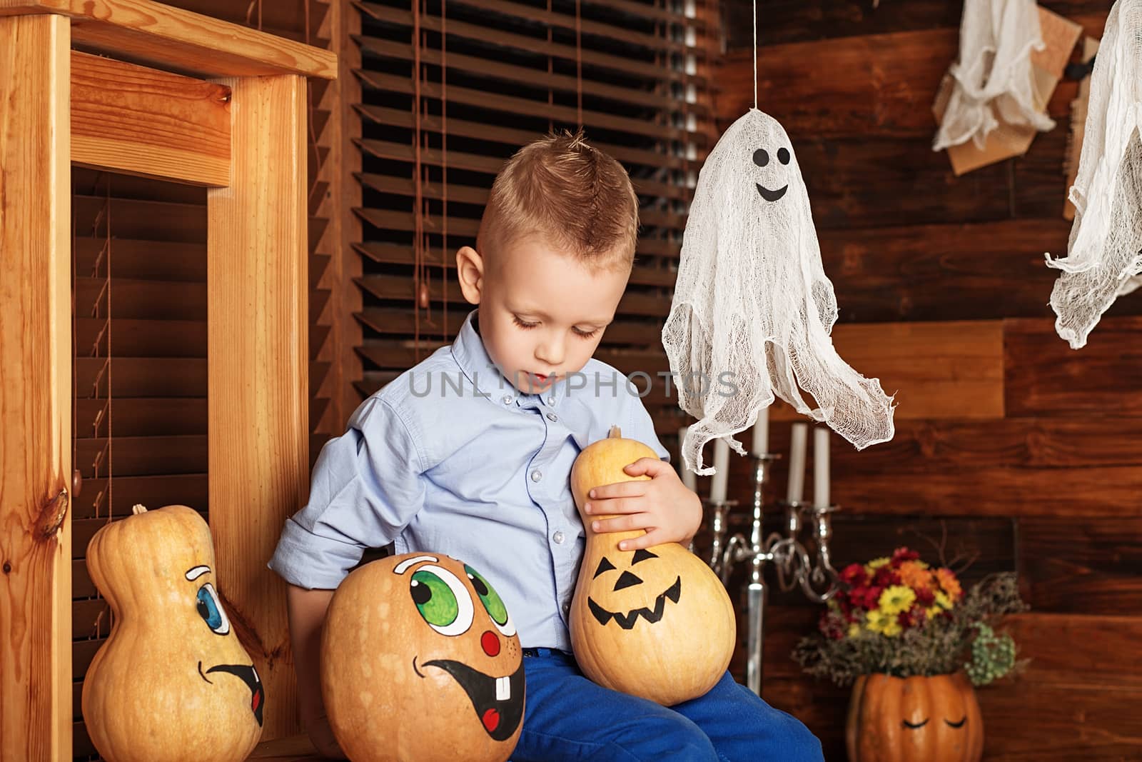 Cute Little Boy having fun in Halloween decorations. Halloween party with child holding painted pumpkin