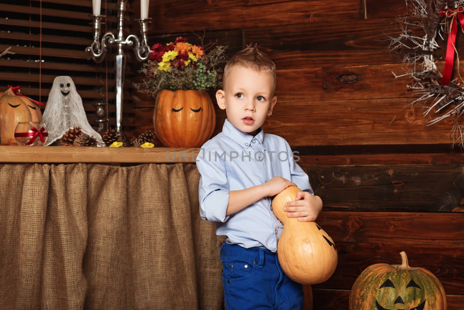 Cute Little Boy having fun in Halloween decorations. Halloween party with child holding painted pumpkin. Your text