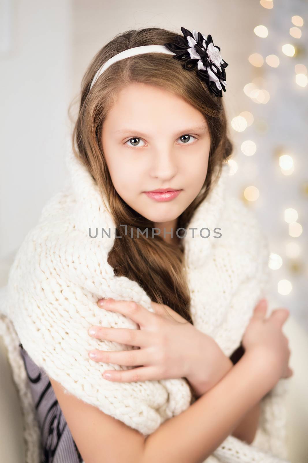 Portrait of a pretty smiling teen girl wrapped in a warm knitted sweater in interior with Christmas decorations