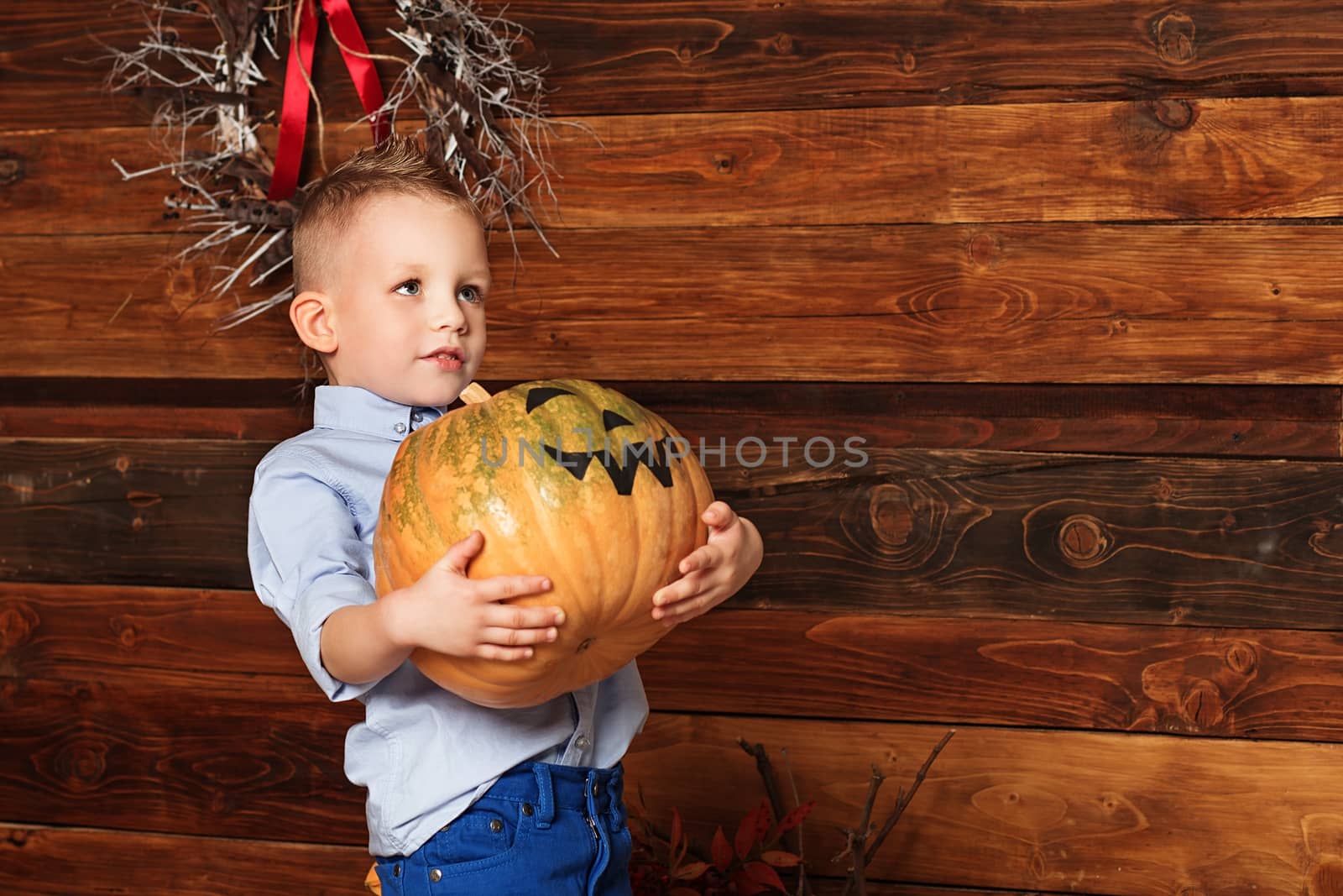 Halloween party with child holding painted pumpkin. Cute Little Boy having fun in Halloween decorations