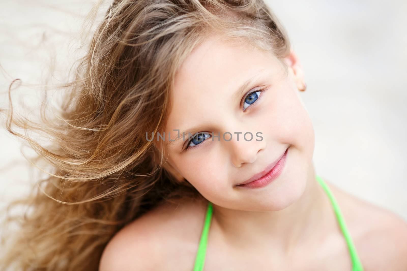 Close-up Portrait of a pretty smiling little girl with waving in the wind long hair sitting on the beach