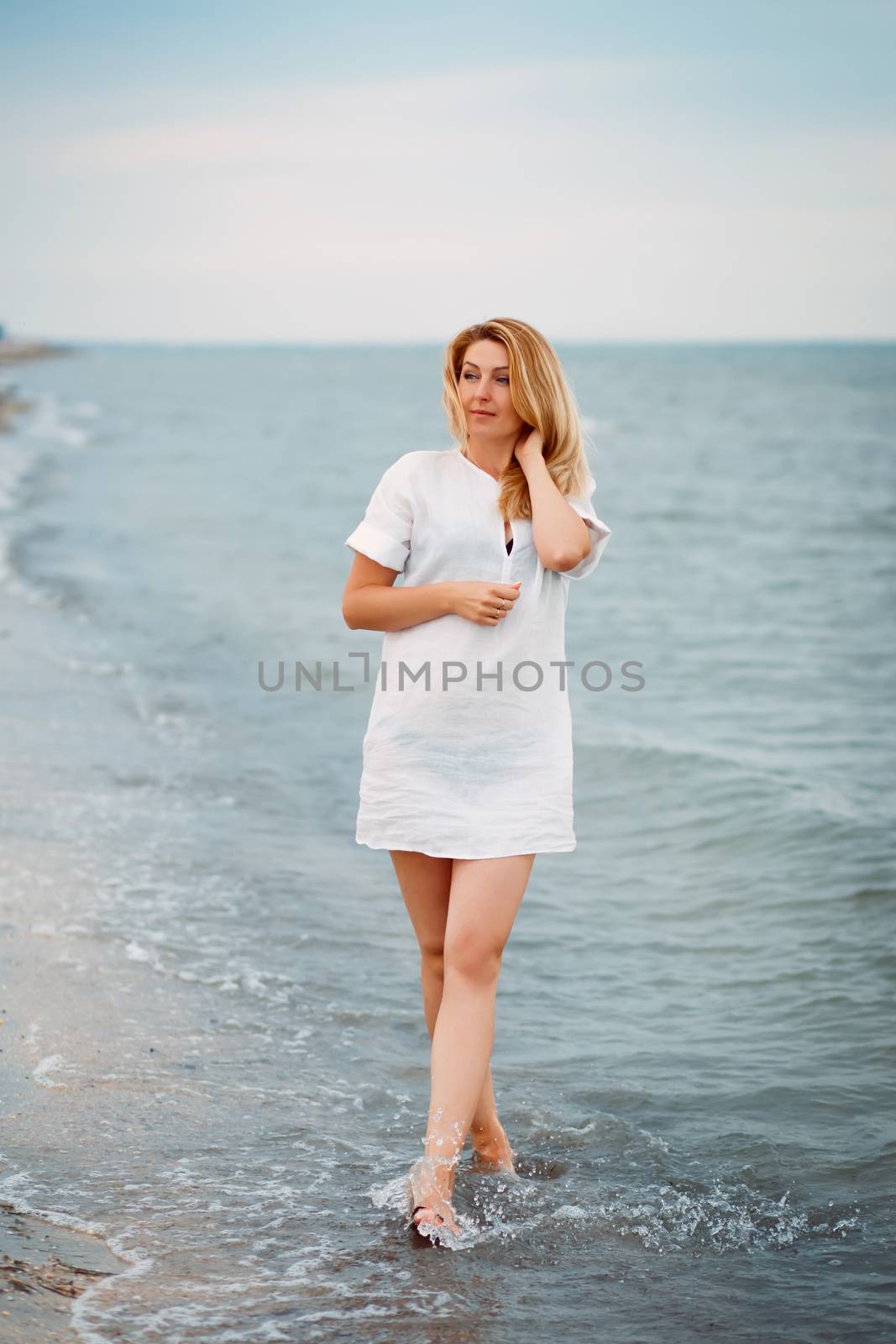 Portrait of a beautiful sexy blond woman walking alone along the beach or ocean warm summer evening
