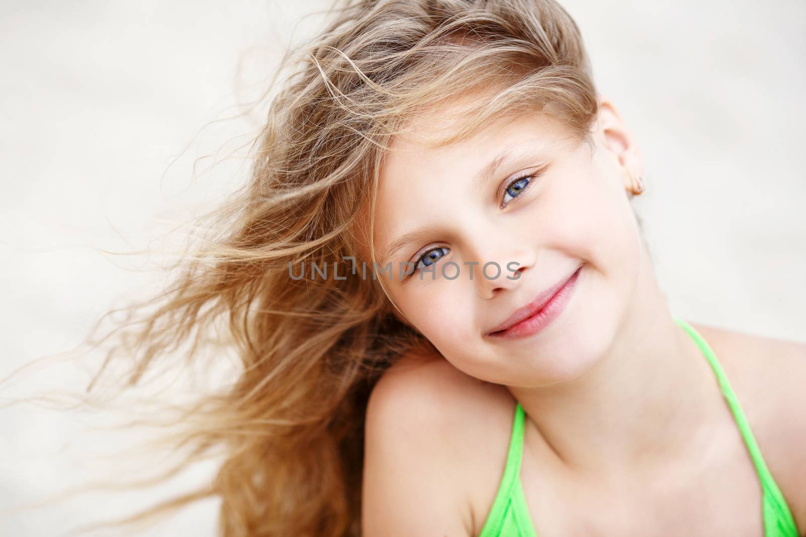 Close-up Portrait of a pretty little girl with waving in the wind long hair sitting on the beach