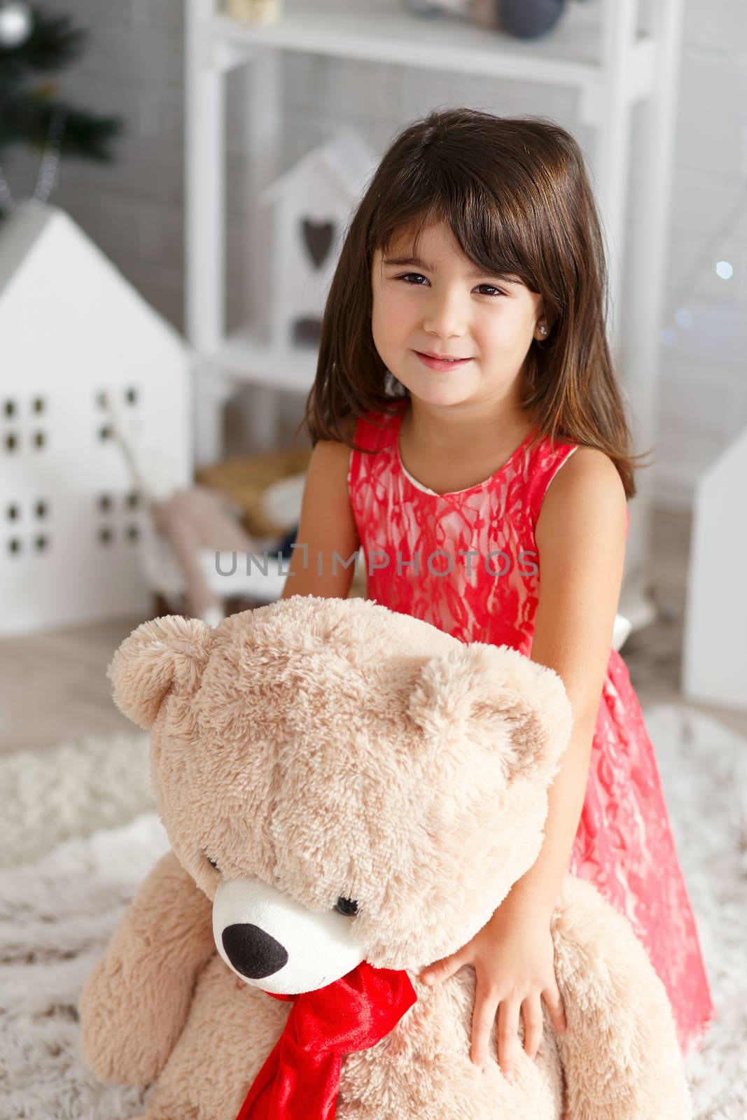 Portrait of a cute little brunette girl hugging a soft big teddy bear in interior with Christmas decorations
