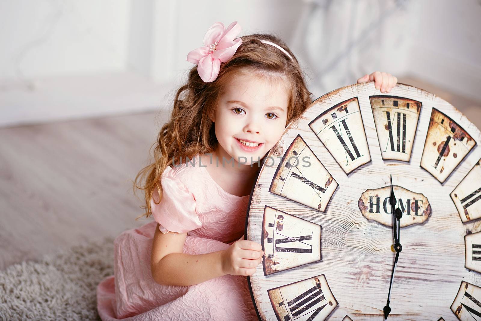 Portrait of Beautiful little girl with long curly hair in pink dress with a big clock waiting for the new year. New year preparation
