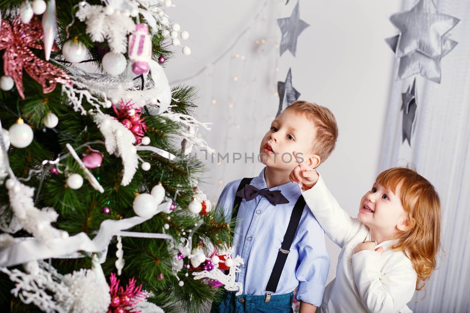 Two little kids decorating Christmas tree with toys, flowers and balls. New year preparation. Happy children and family.