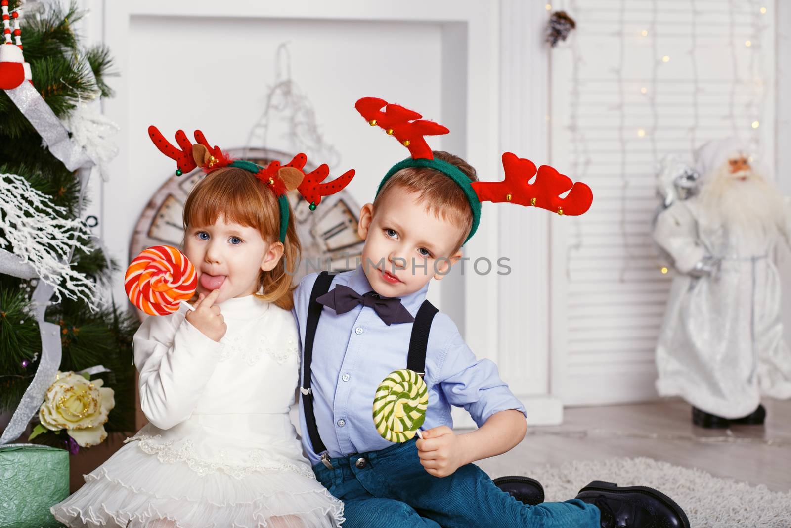 Little girl and boy in reindeer antlers eating a lollipops. Portrait of two funny little kids with a delicious candies in the hands. Christmas and New Year concept. Happy children and family In anticipation of the new year and Christmas.