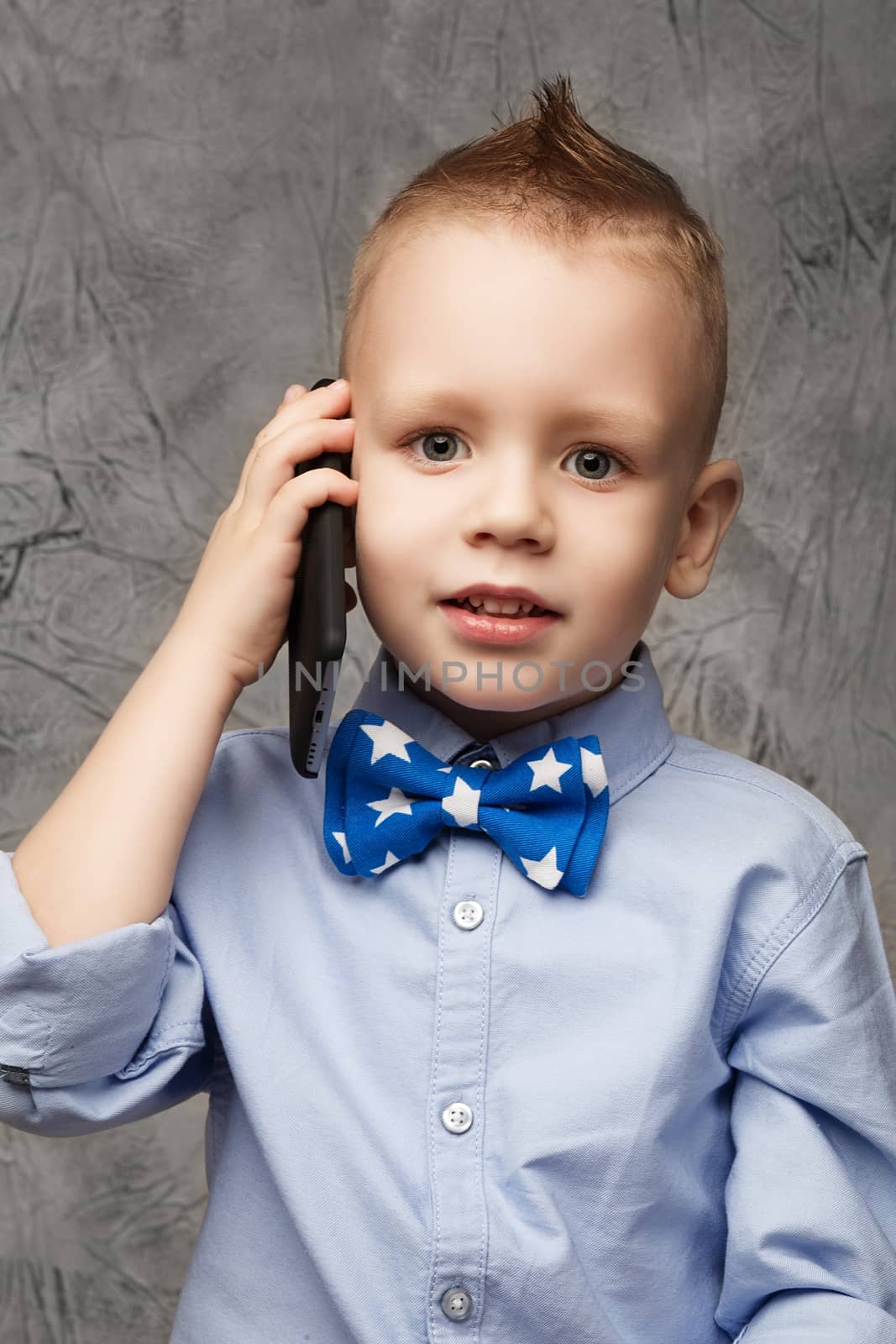 Portrait of little boy in blue shirt and bow tie with mobile pho by natazhekova