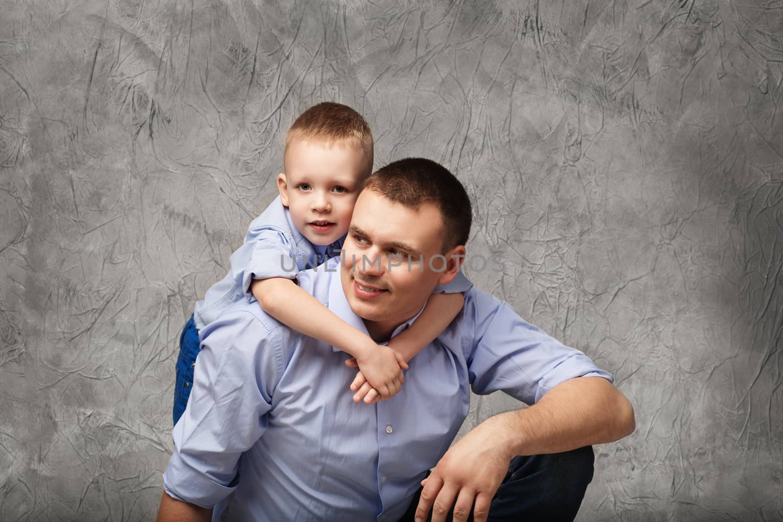 Father and little son in blue shirts in front of gray background by natazhekova