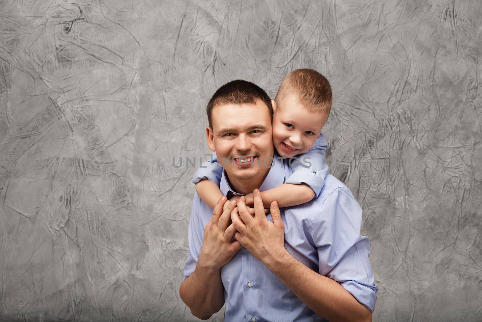 Father and little son in blue shirts in front of gray textured background