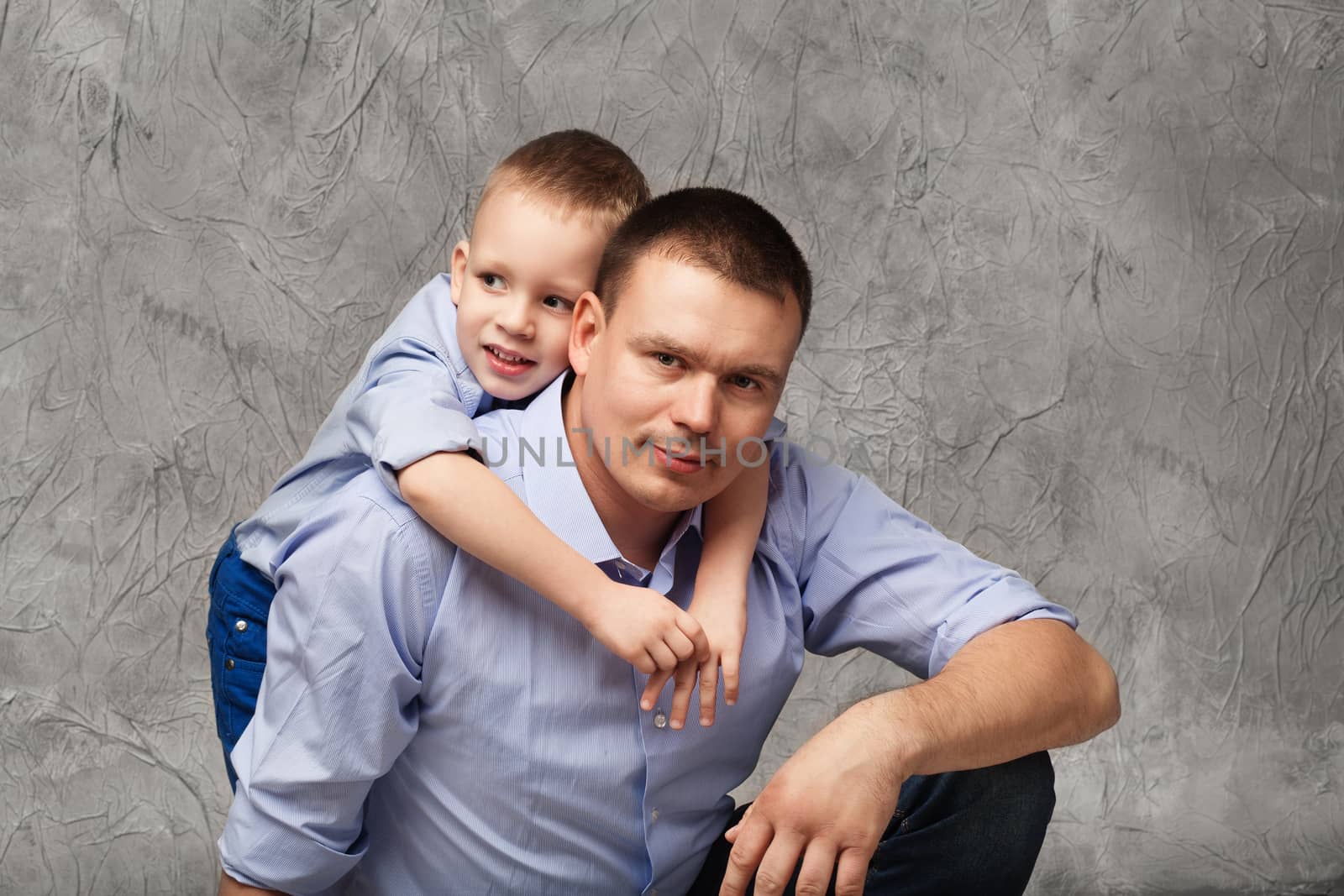 Father and little son in blue shirts in front of gray background by natazhekova