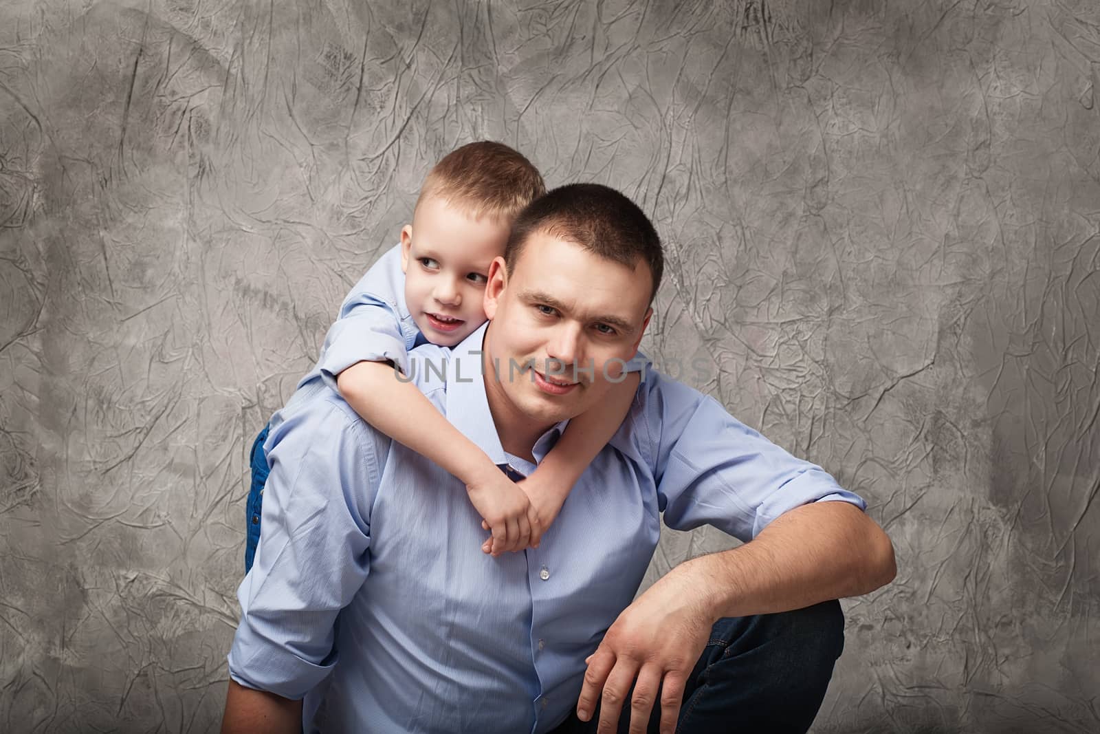 Father and little son in blue shirts in front of gray textured background