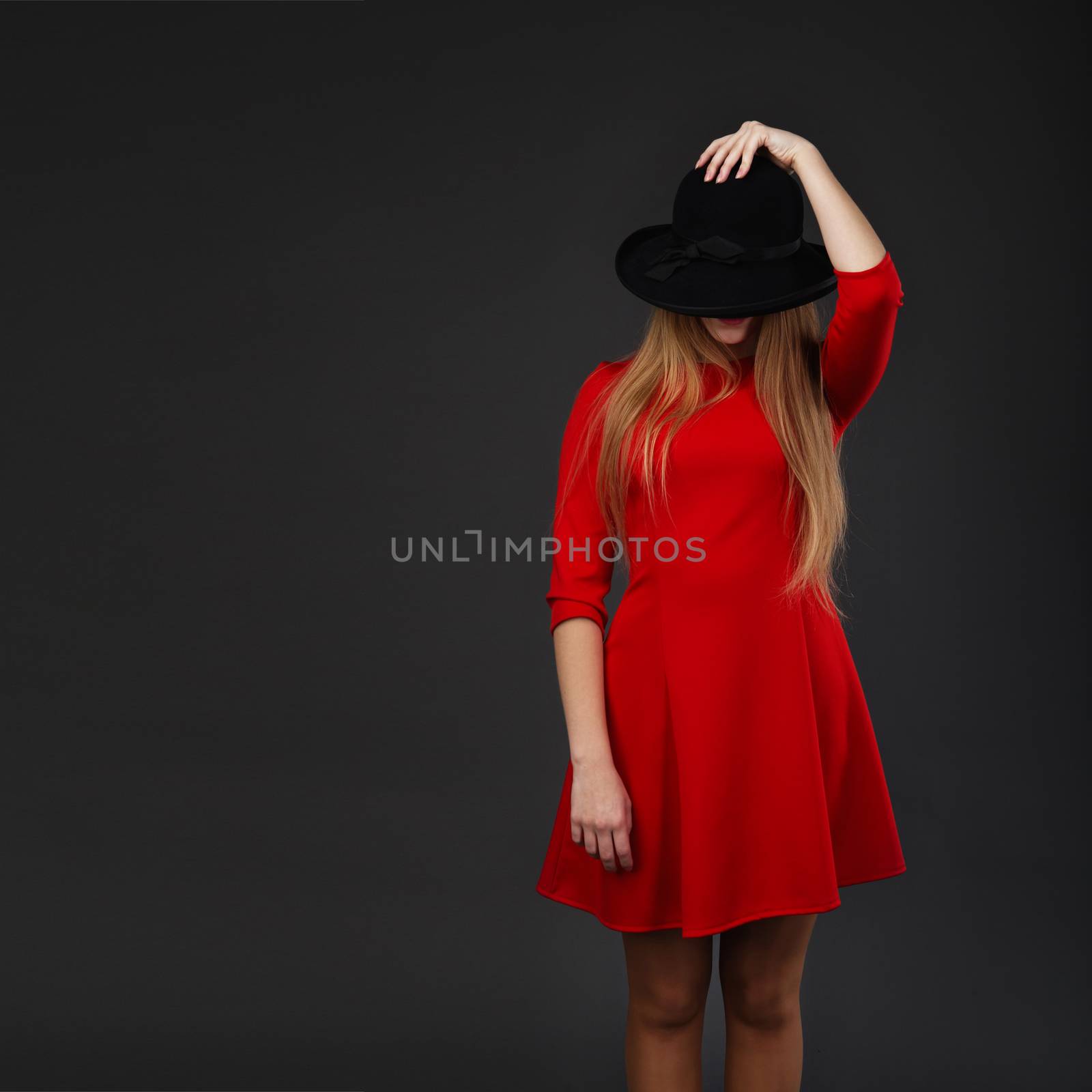 A beautiful girl dressed in red holding her hat. Girl holding hat up to face