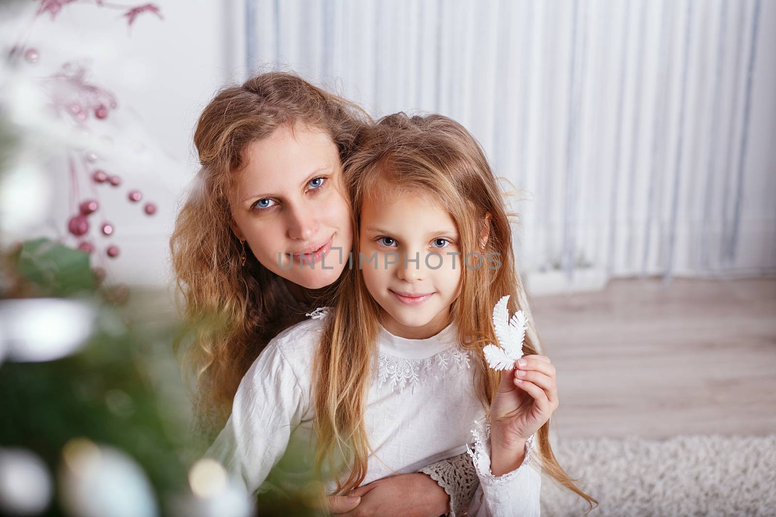 Portrait of happy smiling little girl with mother sitting near Christmas tree.