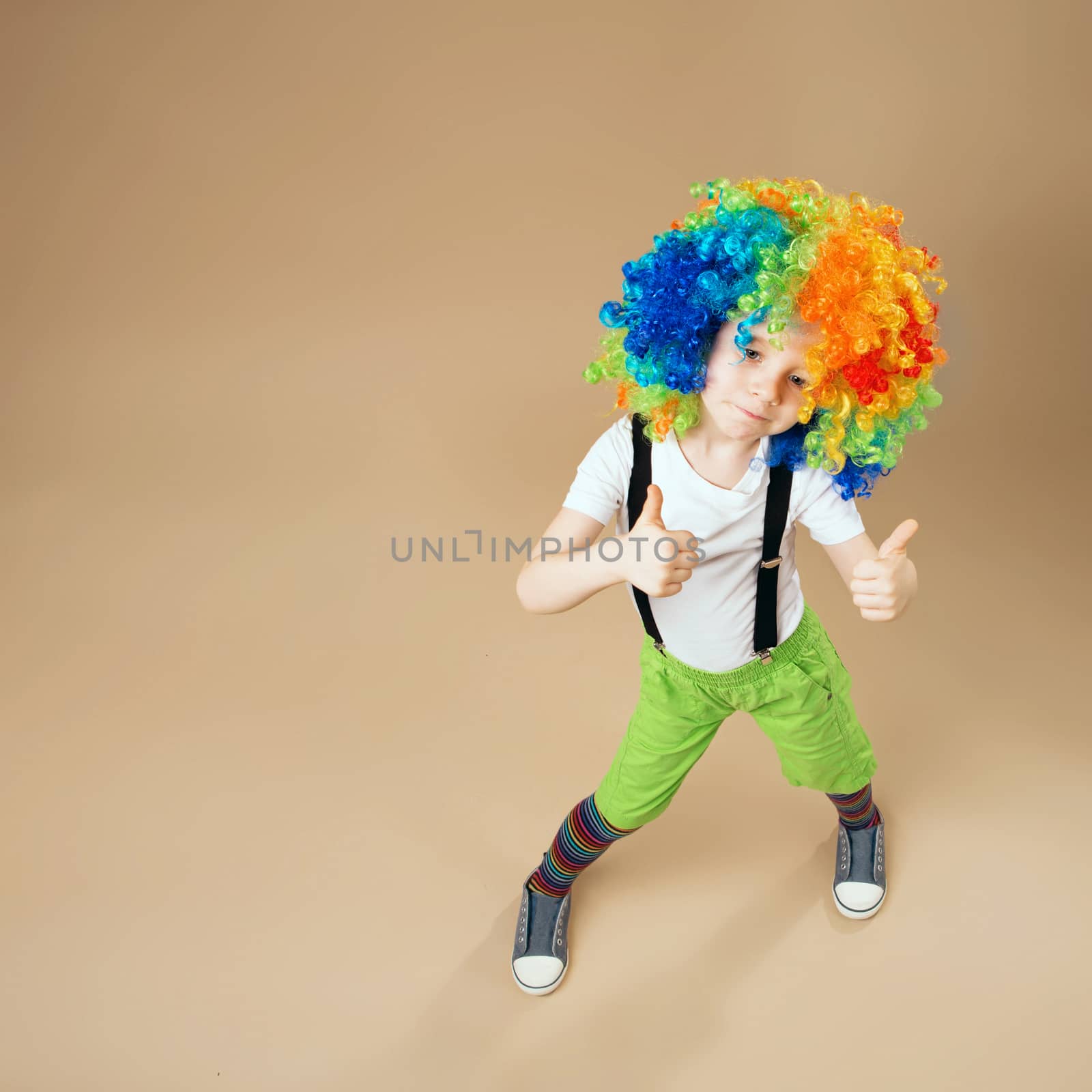 Blithesome children. Happy clown boy with large colorful wig. Little boy in clown wig dancing and having fun. Portrait of a child shot on a wide-angle lens. Birthday boy. Top view portrait