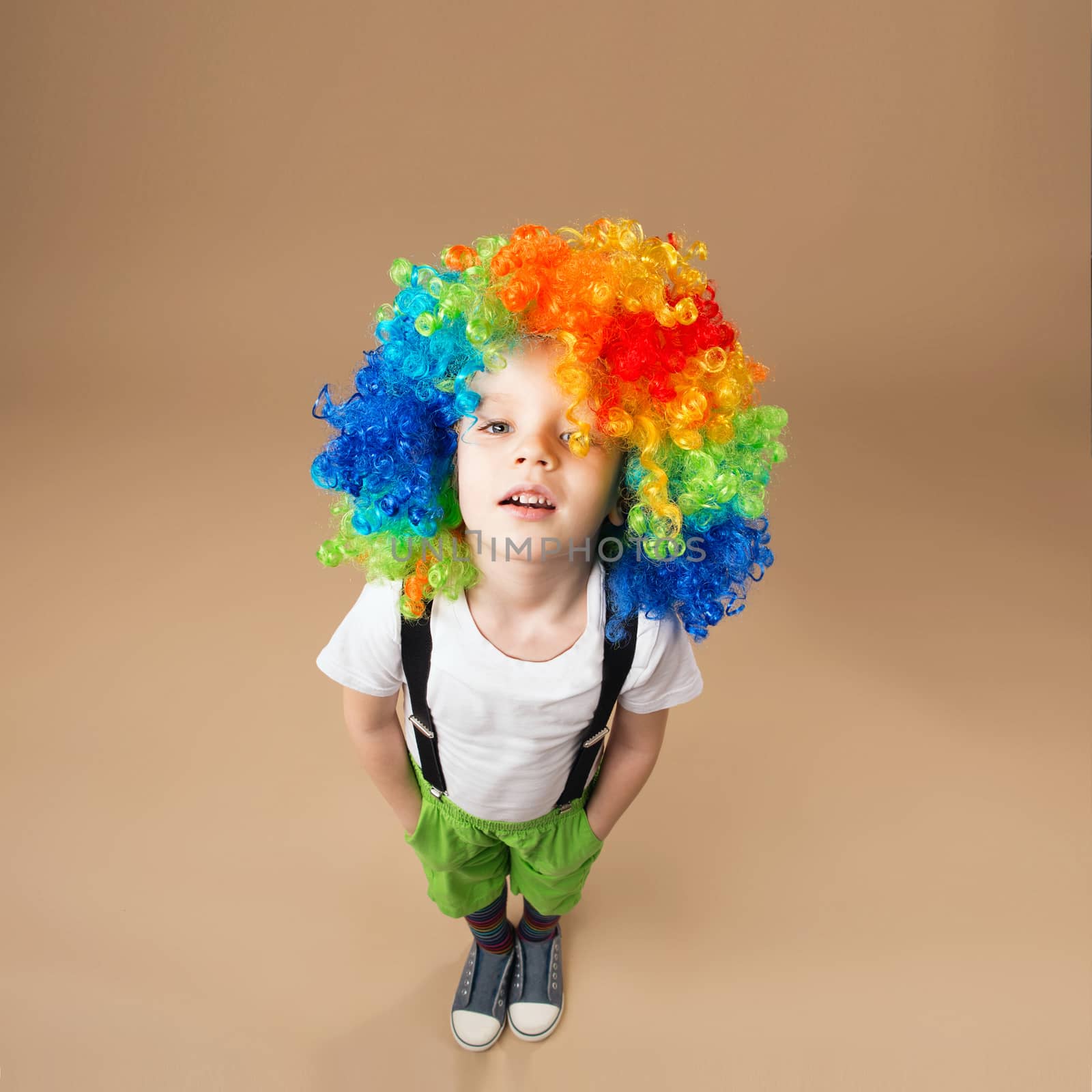 Happy clown boy with large colorful wig. Little boy in clown wig jumping and having fun. Portrait of a child shot on a wide-angle lens. Birthday boy. Positive emotions. Top view portrait