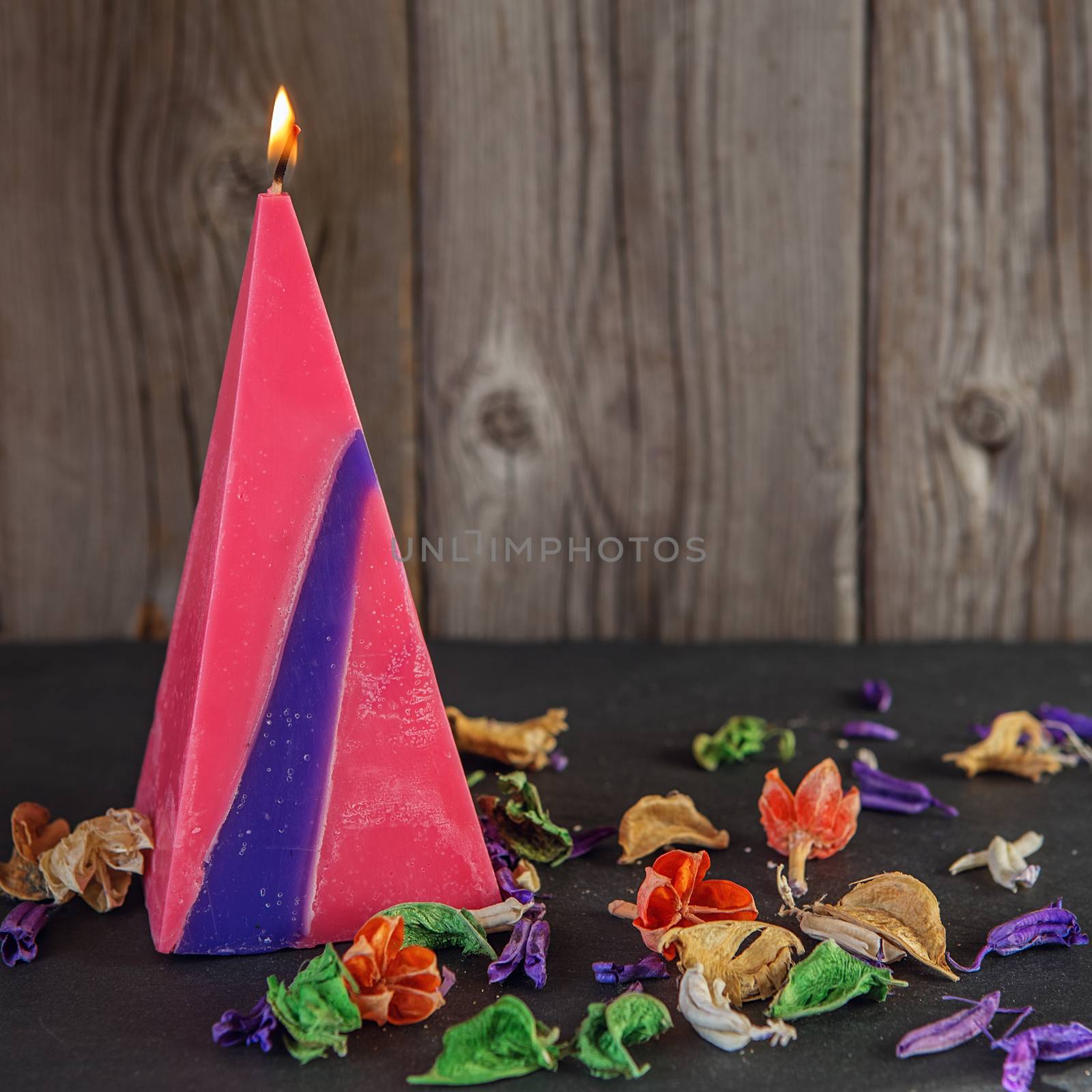 Decorative Handmade candle in the shape of a pyramid among dry flowers on black surface