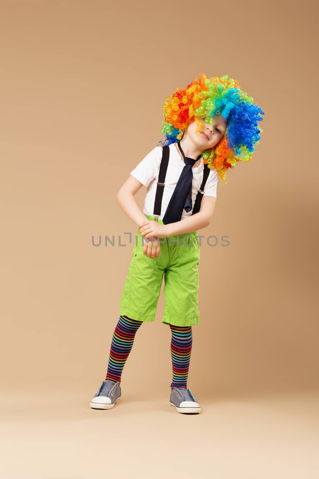 Blithesome children. Happy clown boy with large colorful wig. Little boy in clown wig dancing and having fun. Full-length portrait of Birthday boy.