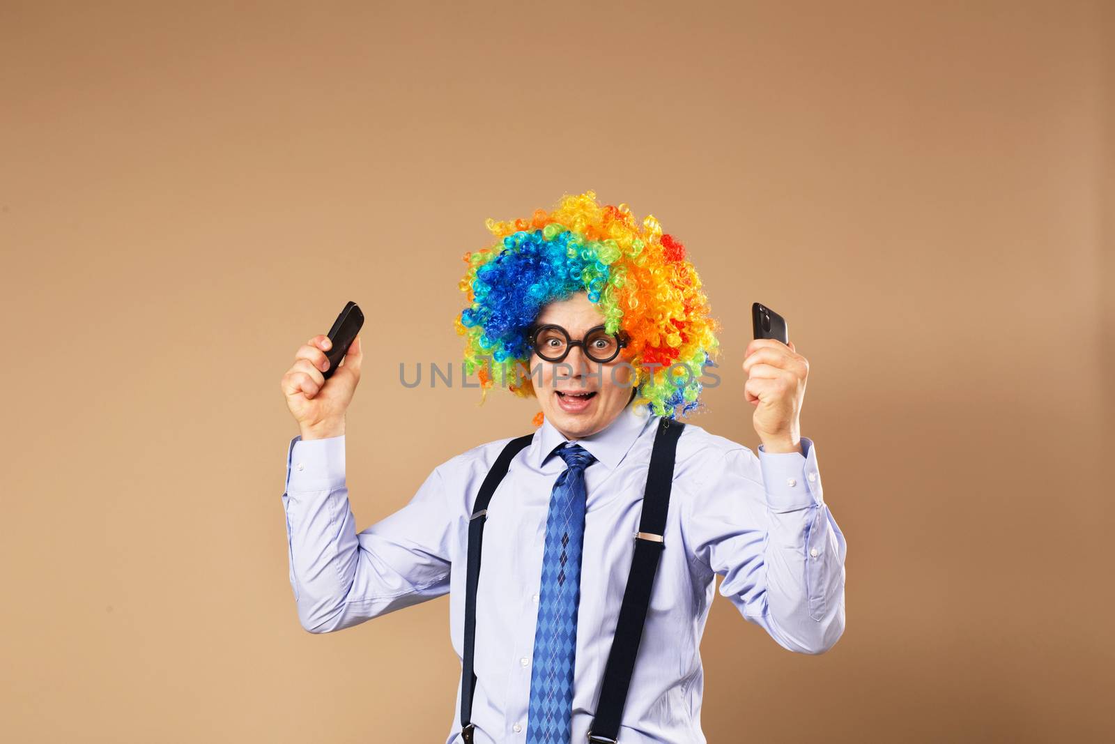 Businessman respond to numerous phone calls. Businessman holding two mobile phones. Close-up Portrait of business man in clown wig. Business concept. Multitasking