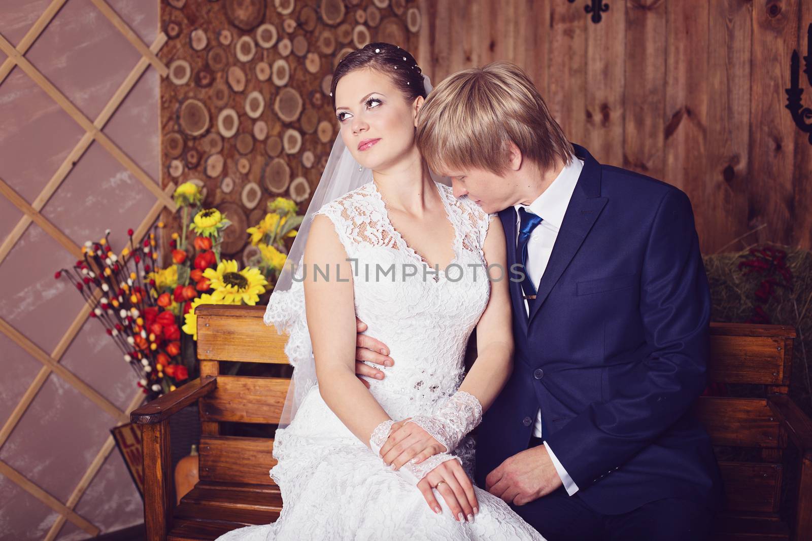 Bride and groom sitting on a bench in studio with vintage interior. Photo of happy newlyweds