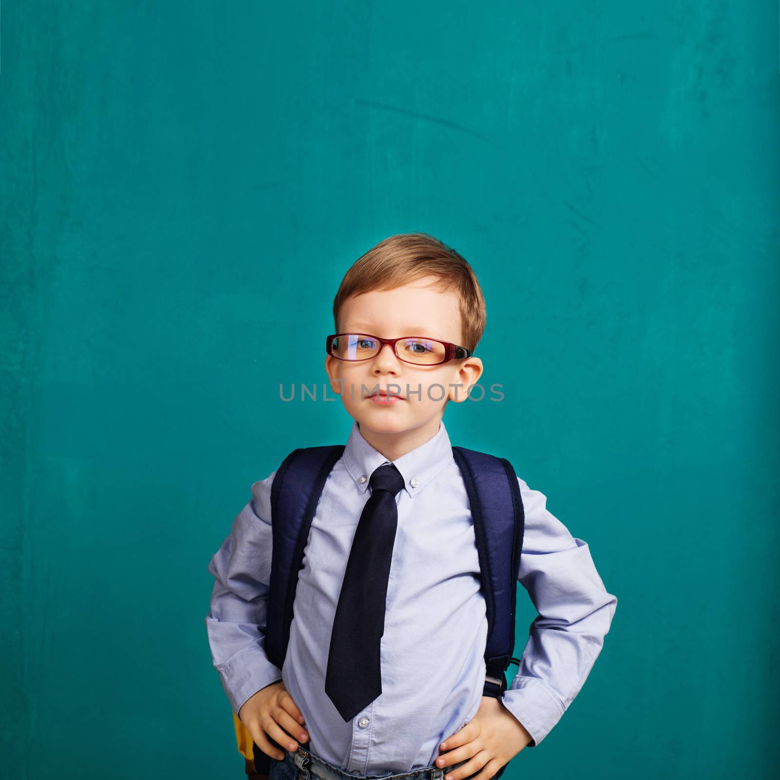 School, kid, rucksack. little Boy in eyeglasses. Cheerful smiling little kid with big backpack against chalkboard. Looking at camera. School concept. Back to School
