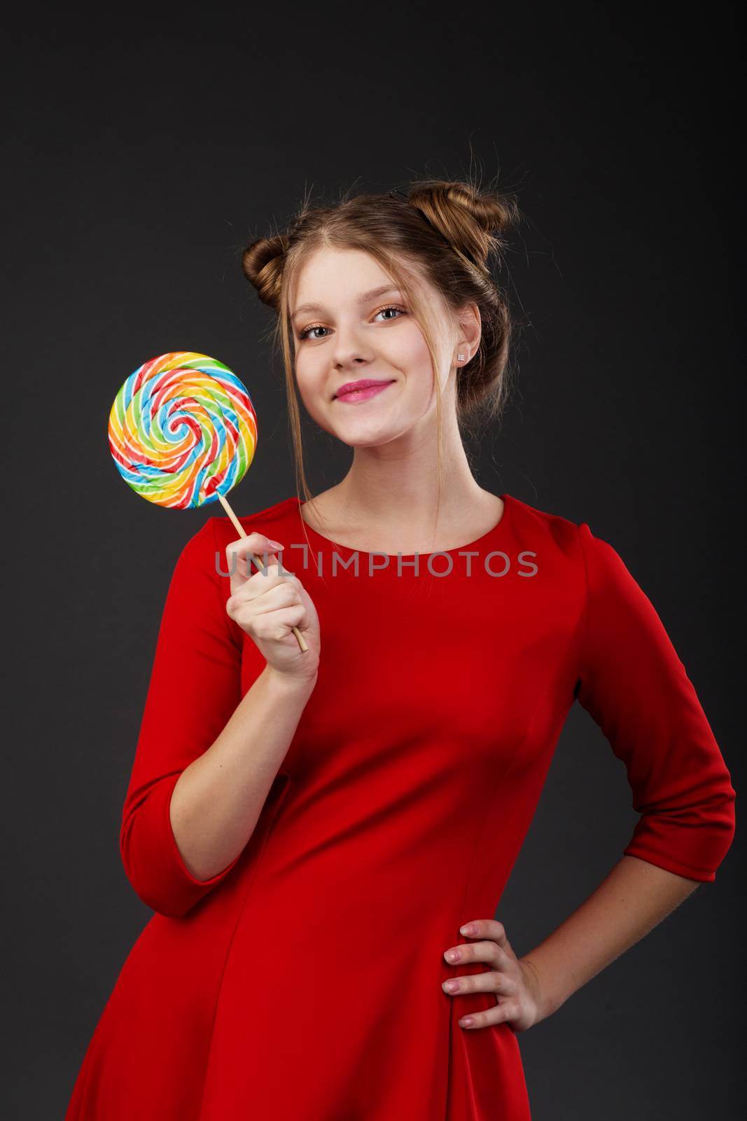 Portrait of a smiling young beautiful girl in a red dress with a big candy. Funny girl with a lollipop