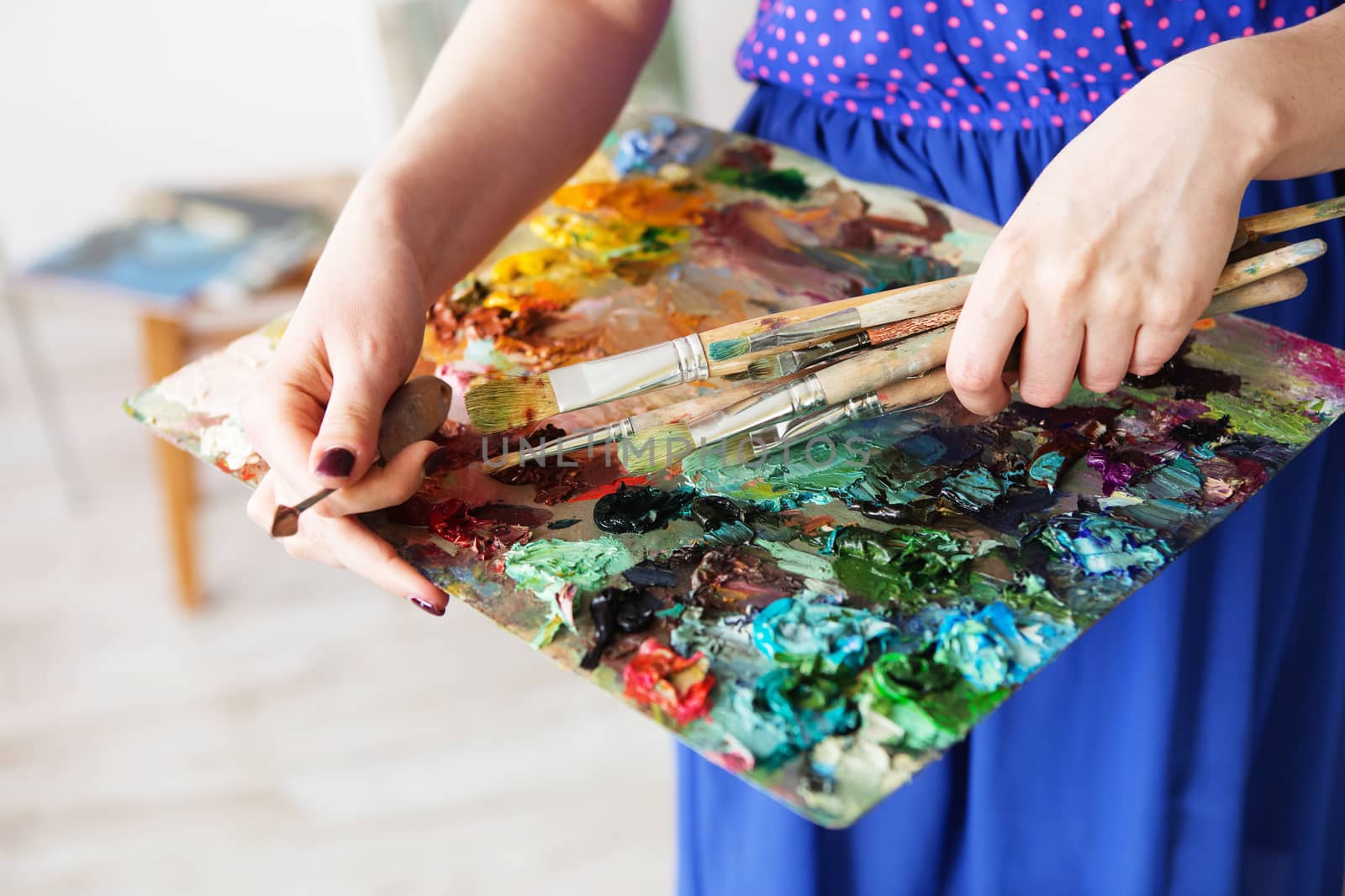 artists brushes and oil paints on wooden palette. macro artist's palette, texture mixed oil paints in different colors and saturation. palette with paintbrush and palette-knife in artist’s hands. The girl artist holding a palette with oil paints