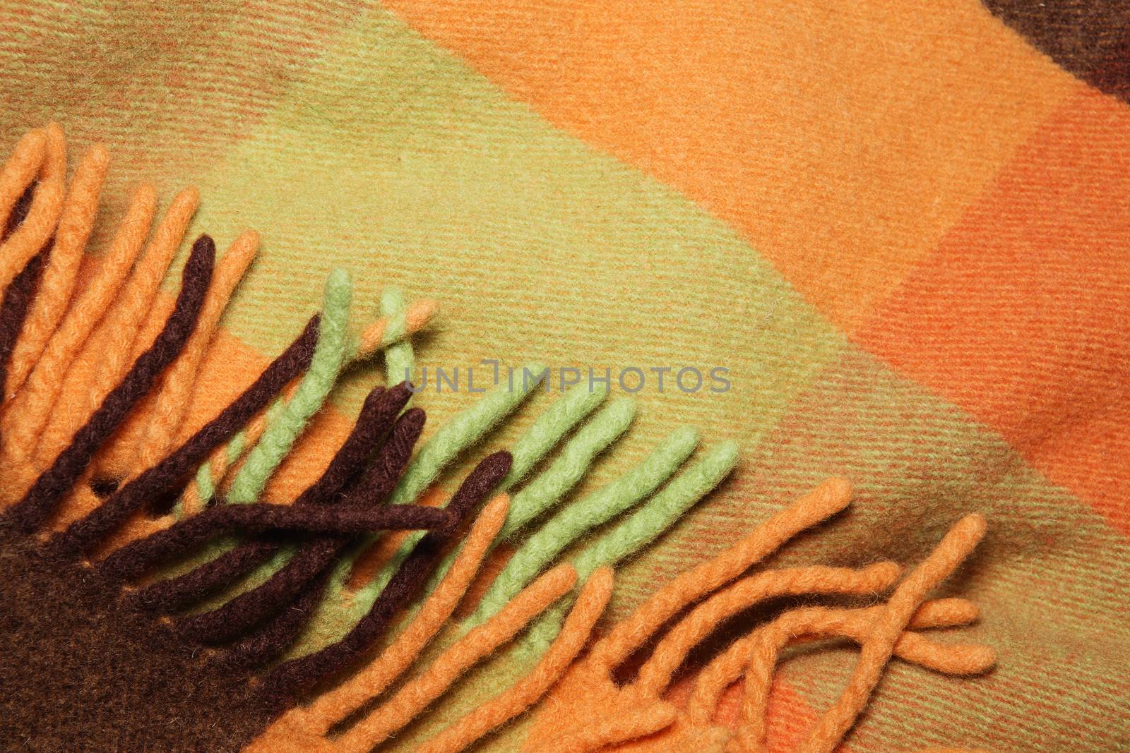 Soft and warm folded alpaca wool blanket with fringe. Green and orange wool plaid texture macro shot. Wool plaid texture with fringe. Wool blanket