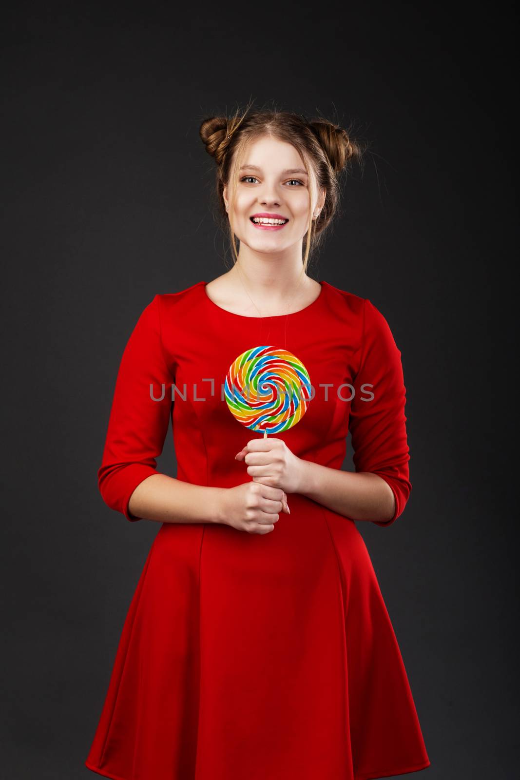 Portrait of a smiling young beautiful girl in a red dress with a big candy. Funny girl with a lollipop