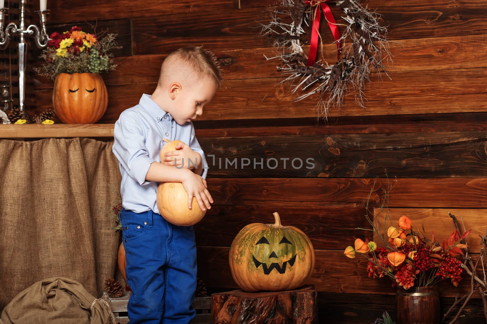 Halloween party with child holding painted pumpkin. Cute Little Boy having fun in Halloween decorations