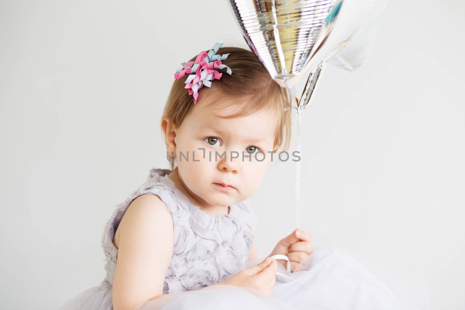 Portrait of a lovely little girl wearing elegant gray dress in front of a white background. Little princess. Little baby girl holding silver star-shaped balloon.