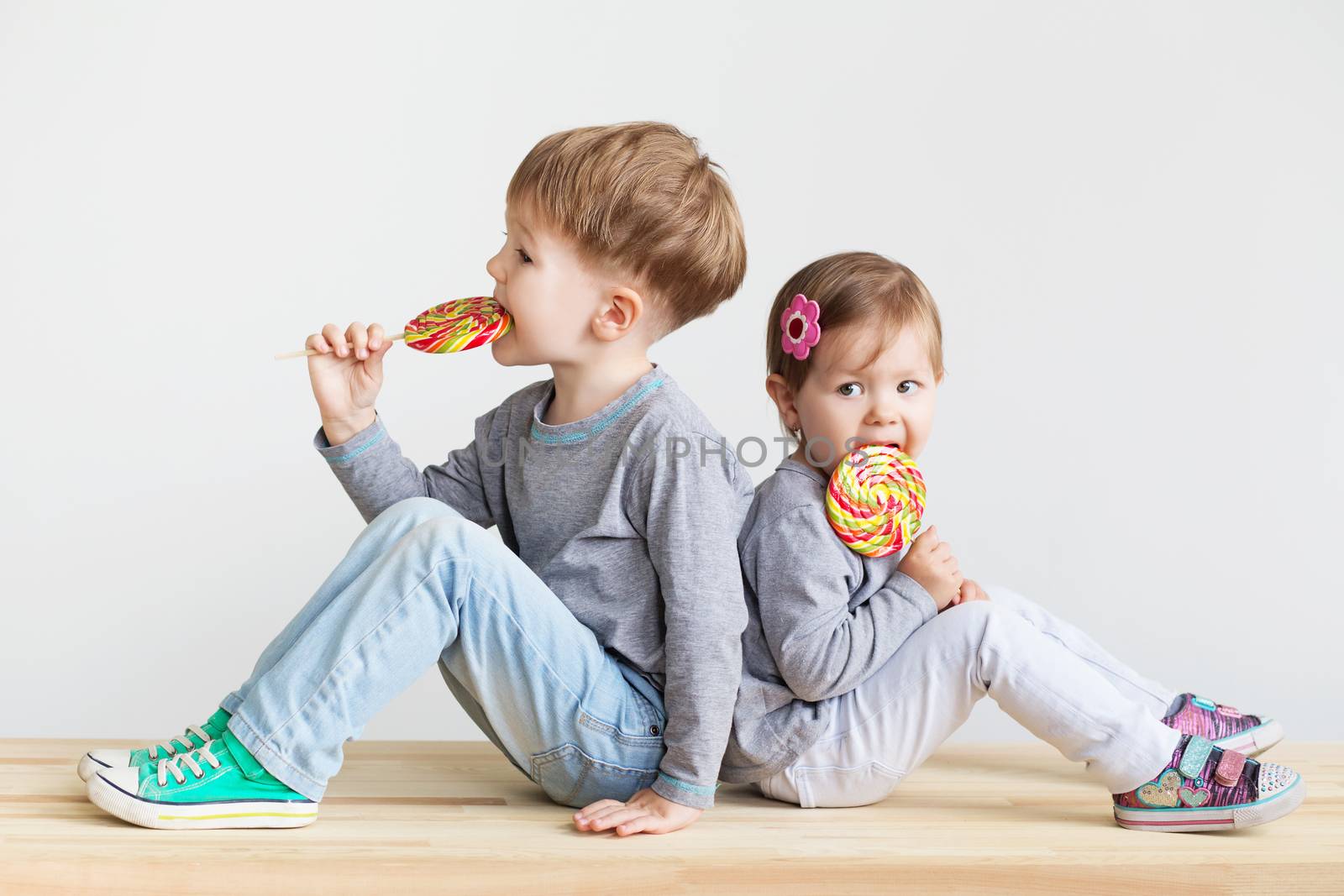 Little children eating lollipops. Happy kids with a big candy. Portrait of a happy little children - boy and girl. Beautiful kids against a white background