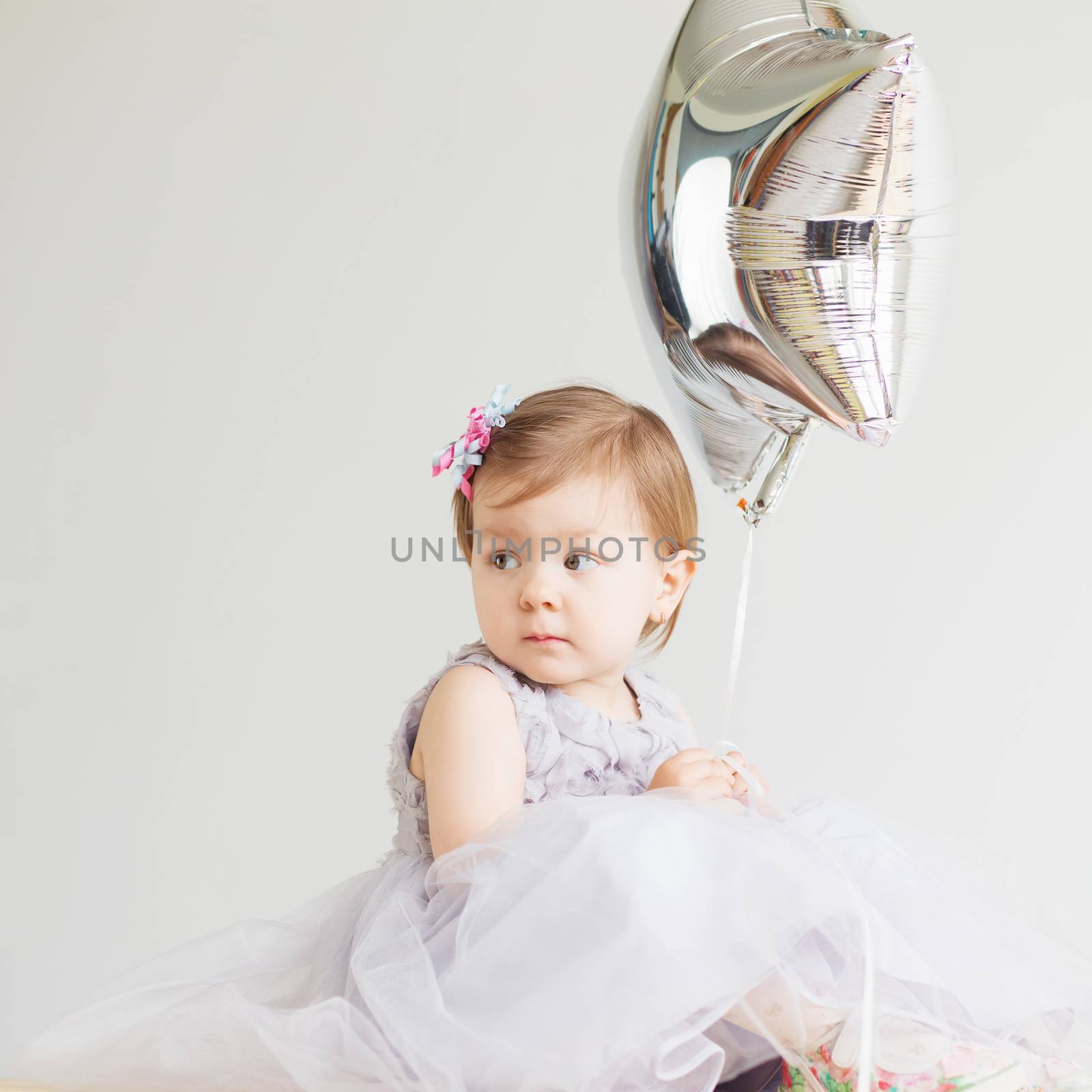 Portrait of a lovely little girl wearing elegant gray dress in front of a white background. Little princess. Little baby girl holding silver star-shaped balloon.