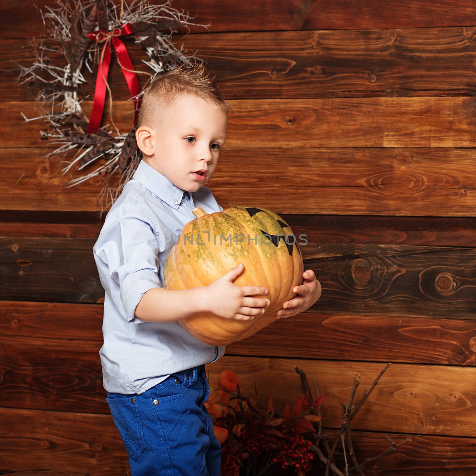 Cute Little Boy having fun in Halloween decorations. Halloween party with child holding painted heavy pumpkin