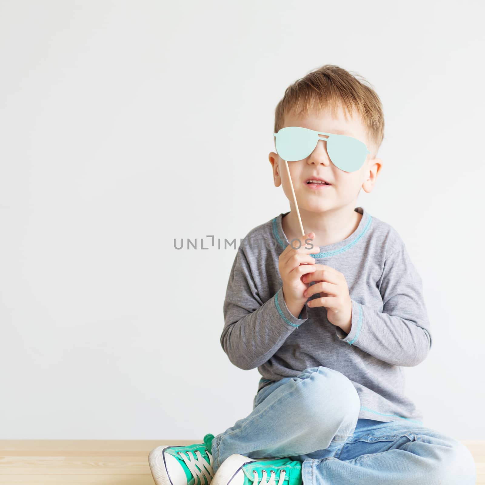 Portrait of a adorable little kid with blue paper glasses against a white background. A blind child