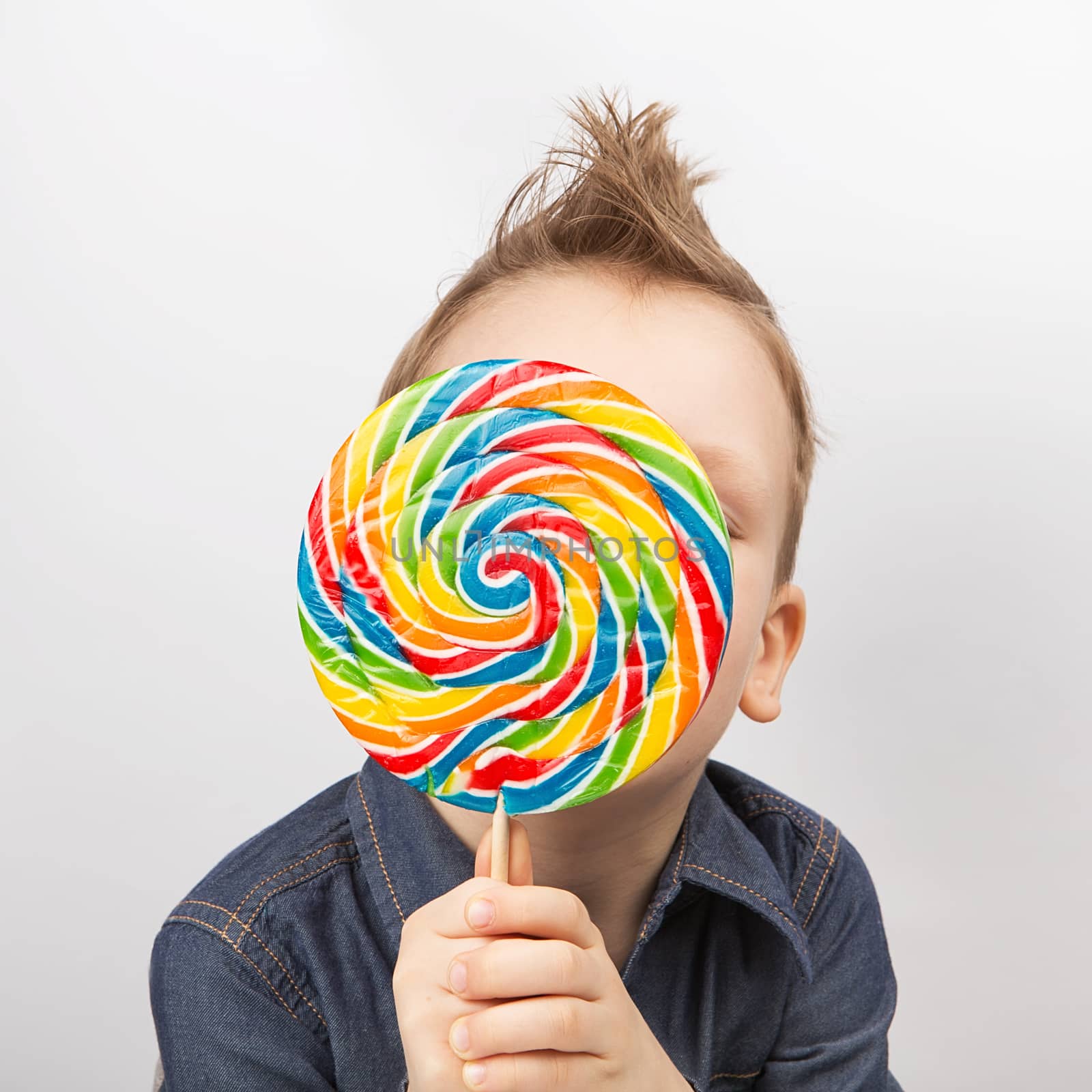 A boy in a denim shirt eating lollipop. Happy kid with a big candy isolated on white background