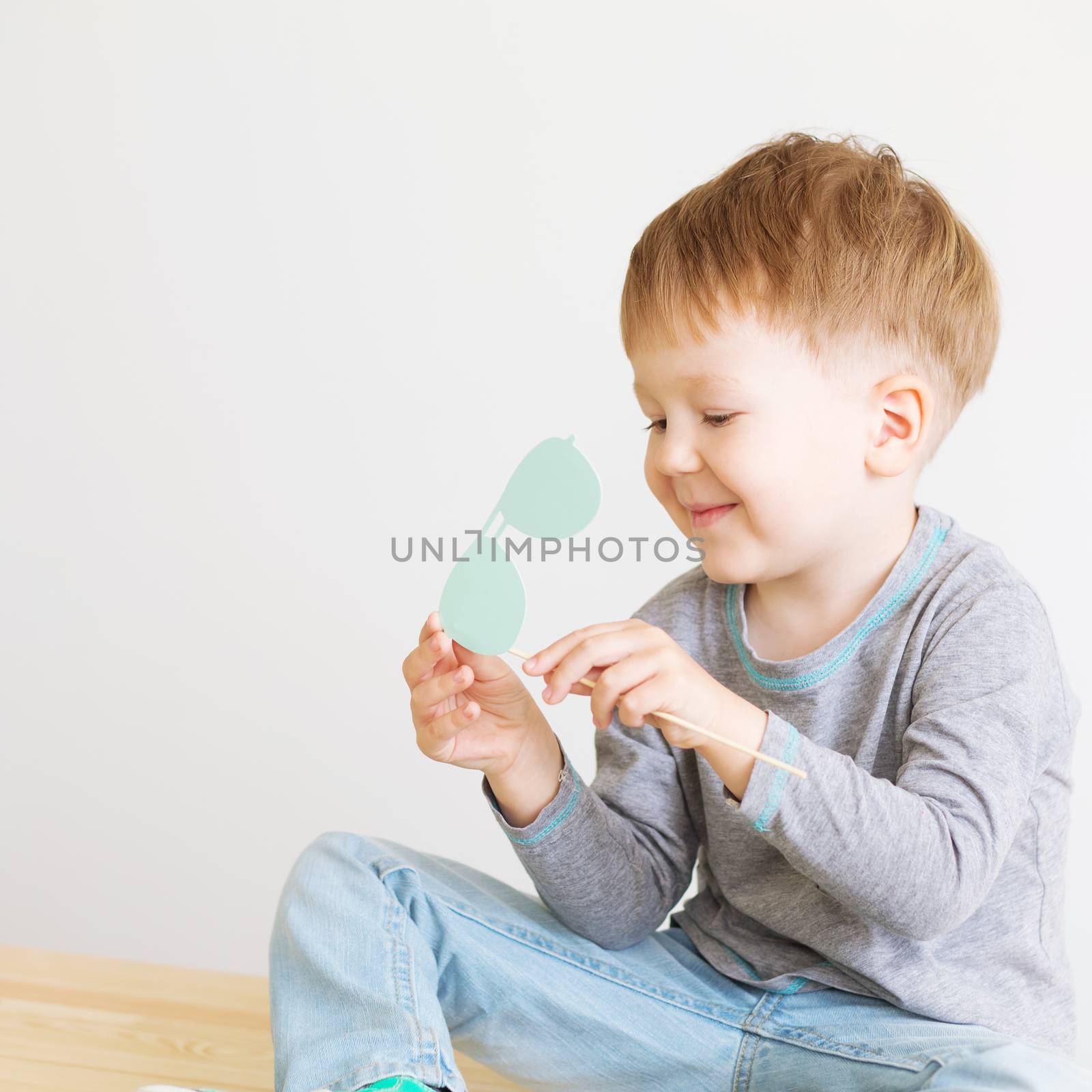 Portrait of a happy adorable little kid with blue paper glasses against a white background. A blind child