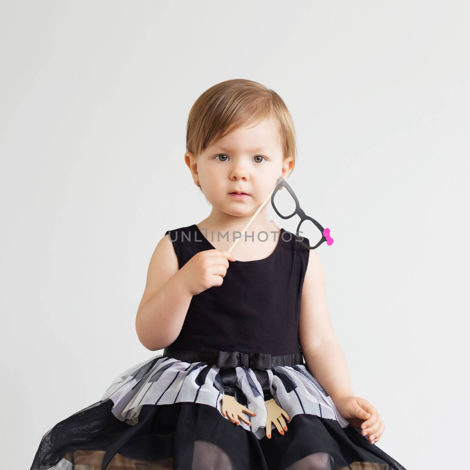 Portrait of a lovely little girl with funny photo props paper glasses against a white background