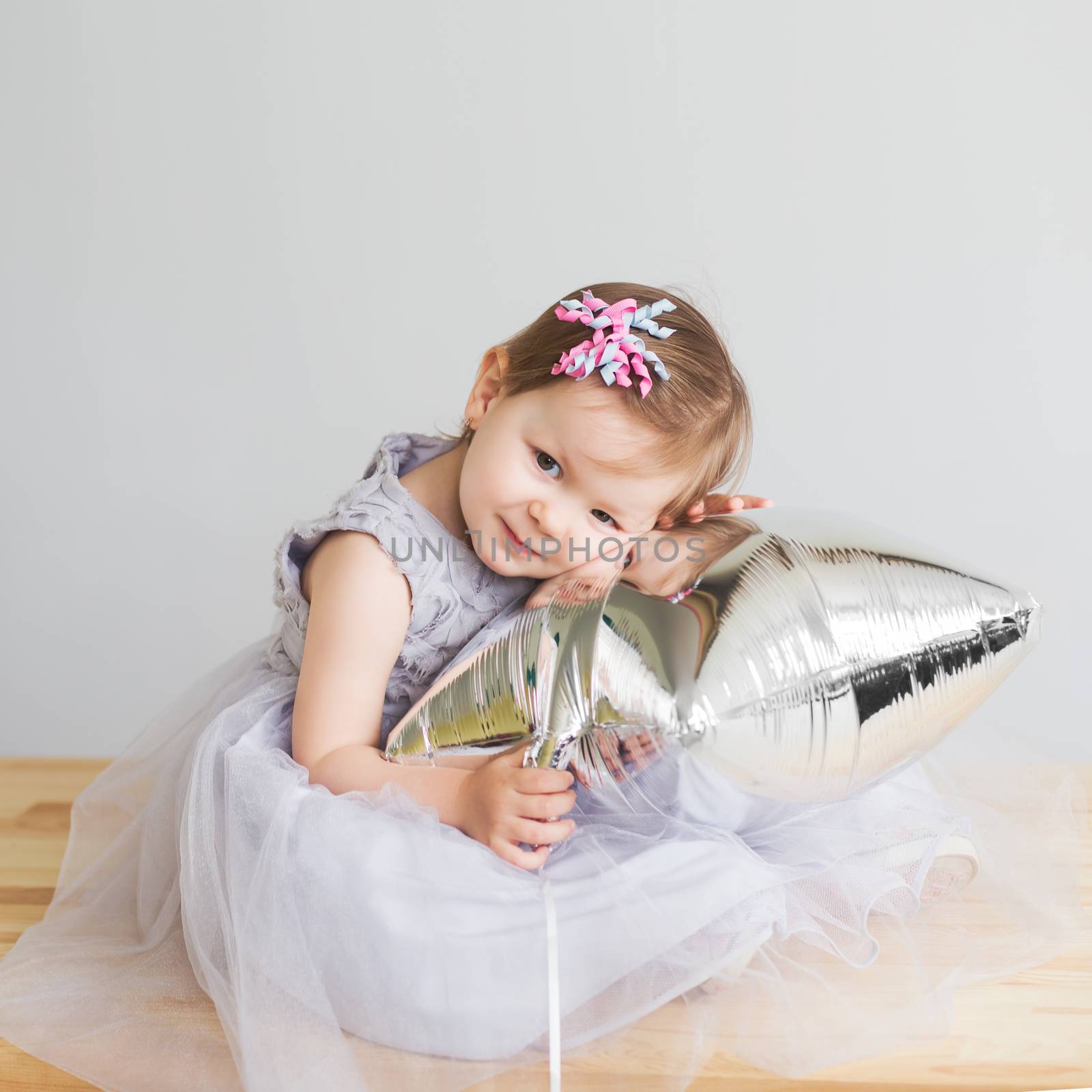 Portrait of a lovely little girl in elegant gray dress in front of a white background. Little princess. Little baby girl playing with silver star-shaped balloon.