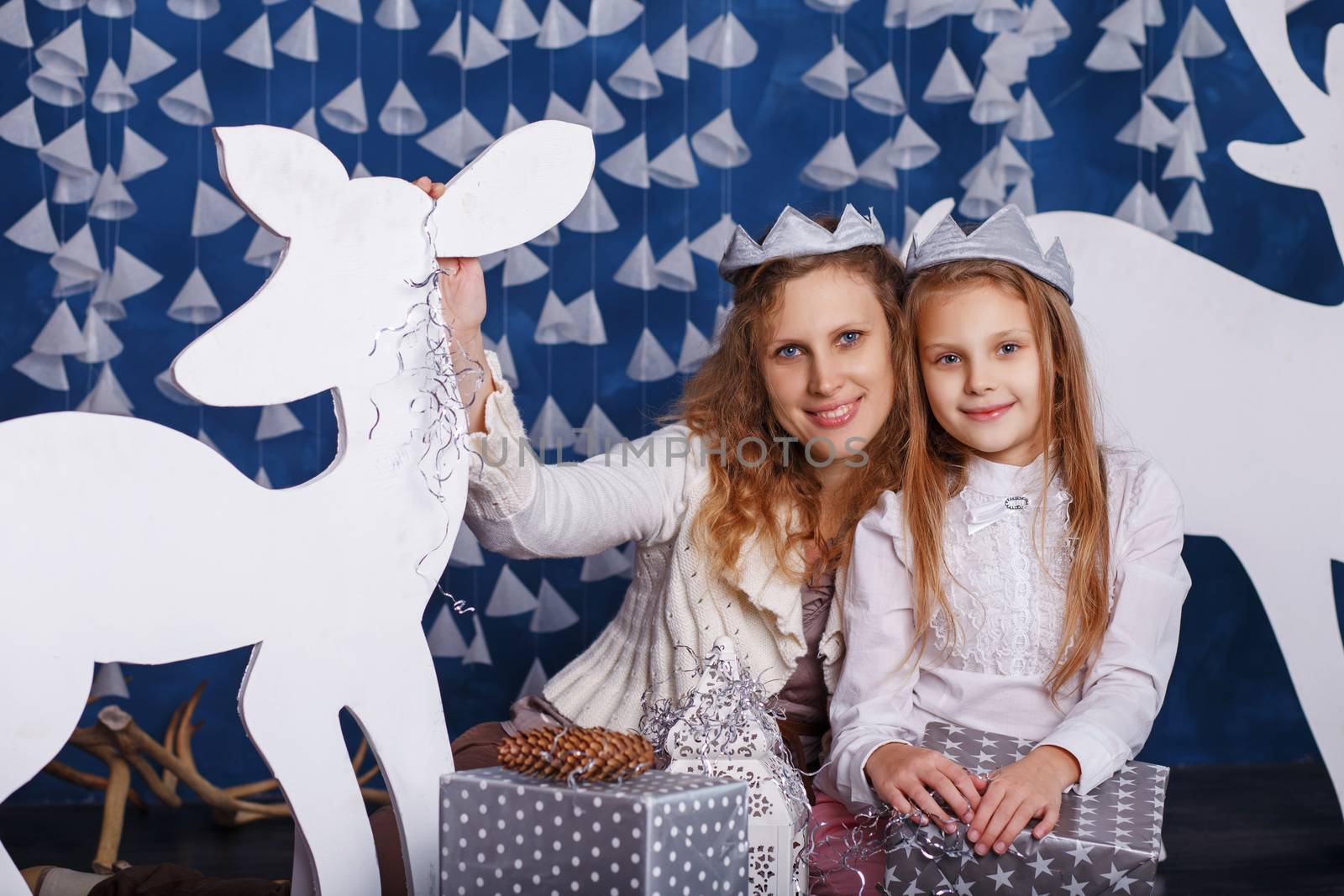 Portrait of happy smiling little girl with mother sitting among Christmas decorations