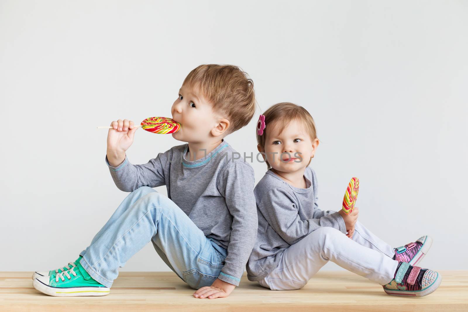 Little children eating lollipops. Happy kids with a big candy. Portrait of a happy little children - boy and girl. Beautiful kids against a white background