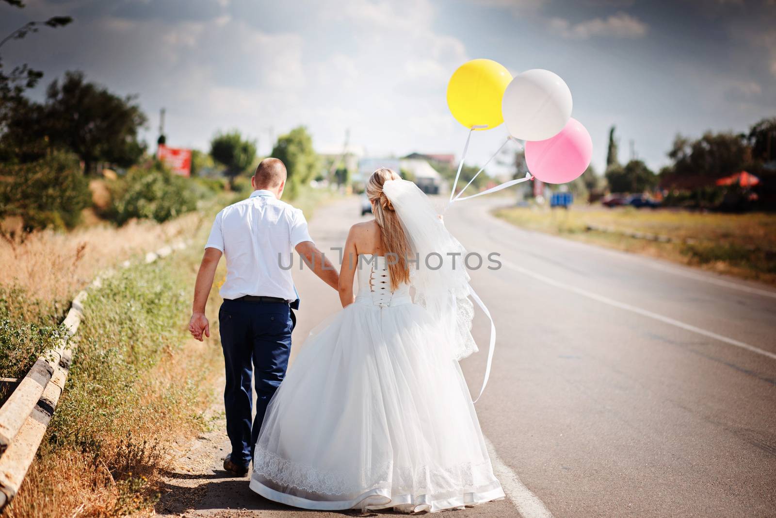 Happy married couple with balloons walk together on the road by natazhekova