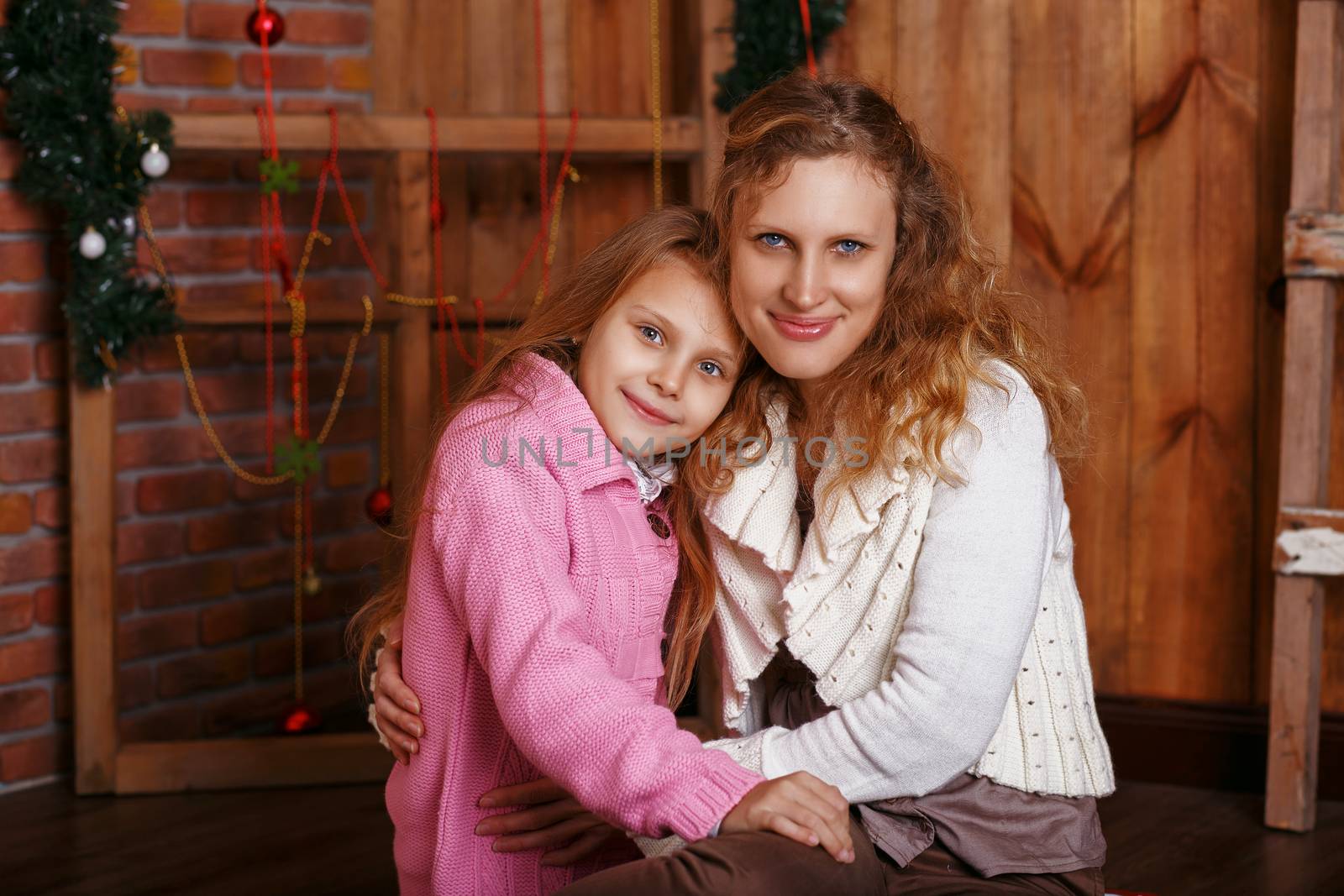 Portrait of happy smiling little girl with mother sitting among Christmas decorations