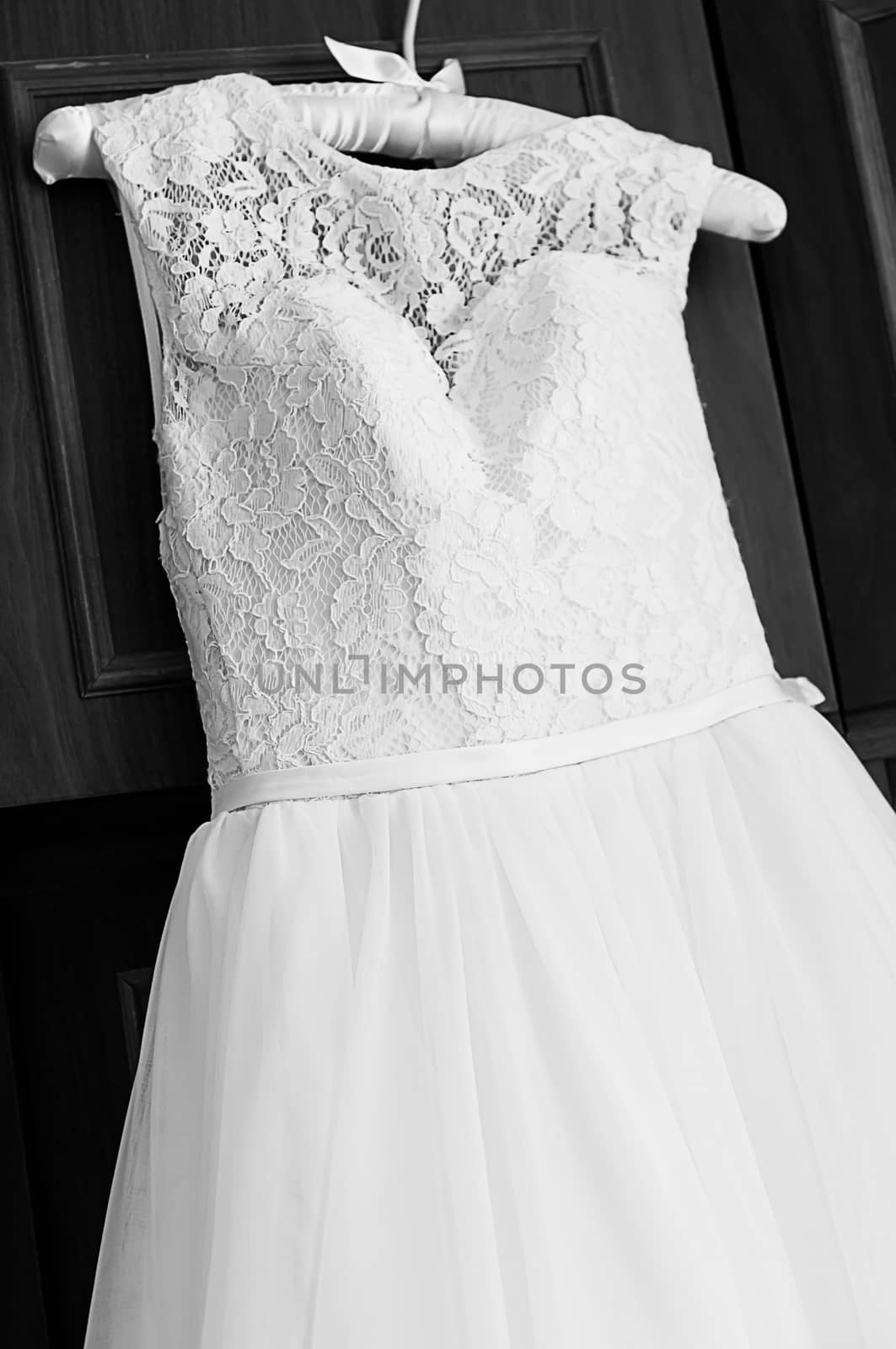 Wedding dress hanging on on the soft tissue hanger. Beautiful female wedding dress with upper part of lace. Black and white photography