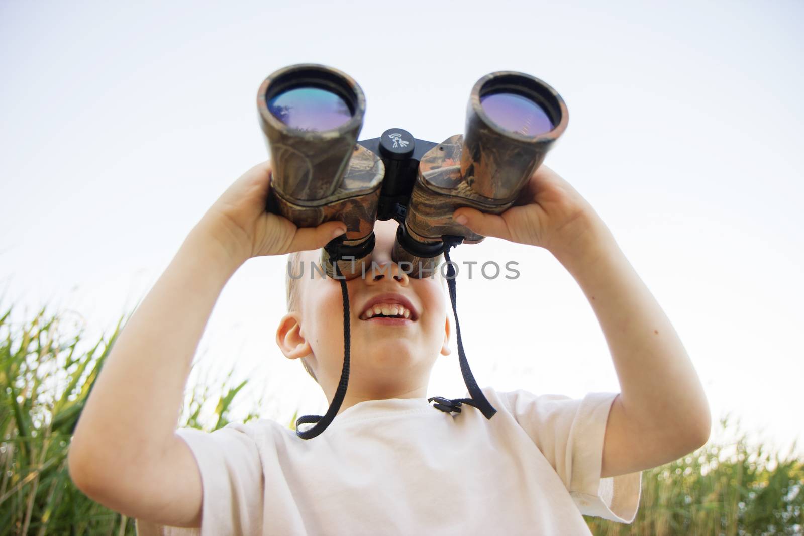 Portrait of little boy looking through binoculars on river bank. Cute kid with binoculars. The boy looks up at the sky through binoculars