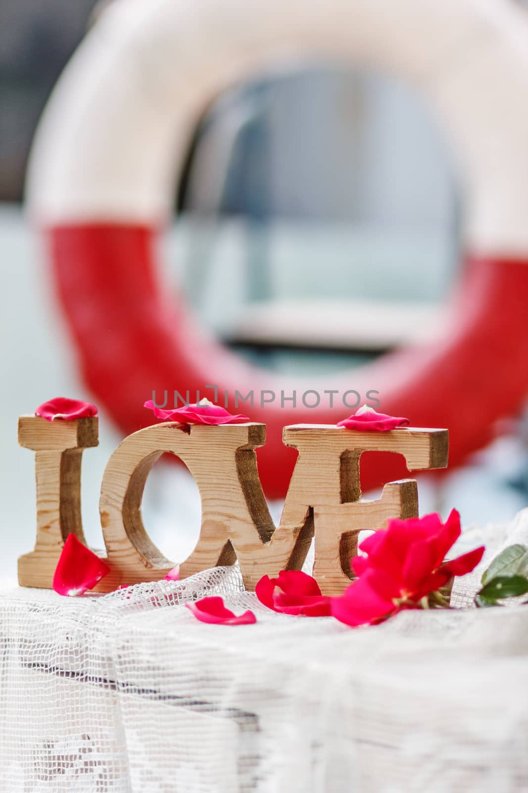 Love saves the world. Valentine's Day. Carved wood word "Love" among pink rose petals on the background of a life buoy