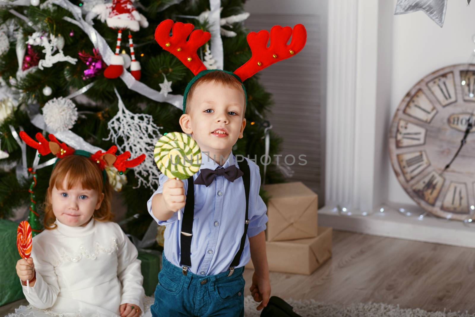 Little girl and boy in reindeer antlers eating a lollipops. Portrait of two funny little kids with delicious candies in the hands. Happy children and family In anticipation of new year and Christmas.