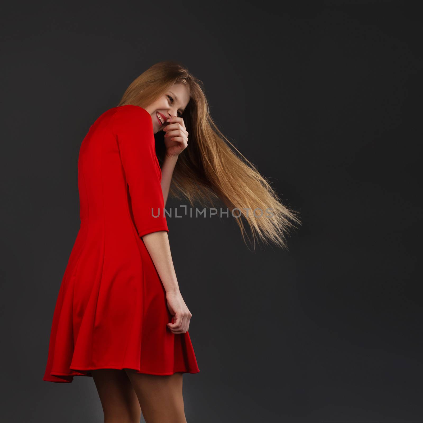 Portrait of a laughing young beautiful girl in a red dress with a flying hair. Girl with long flowing hair. Hair fluttering in motion. Back view