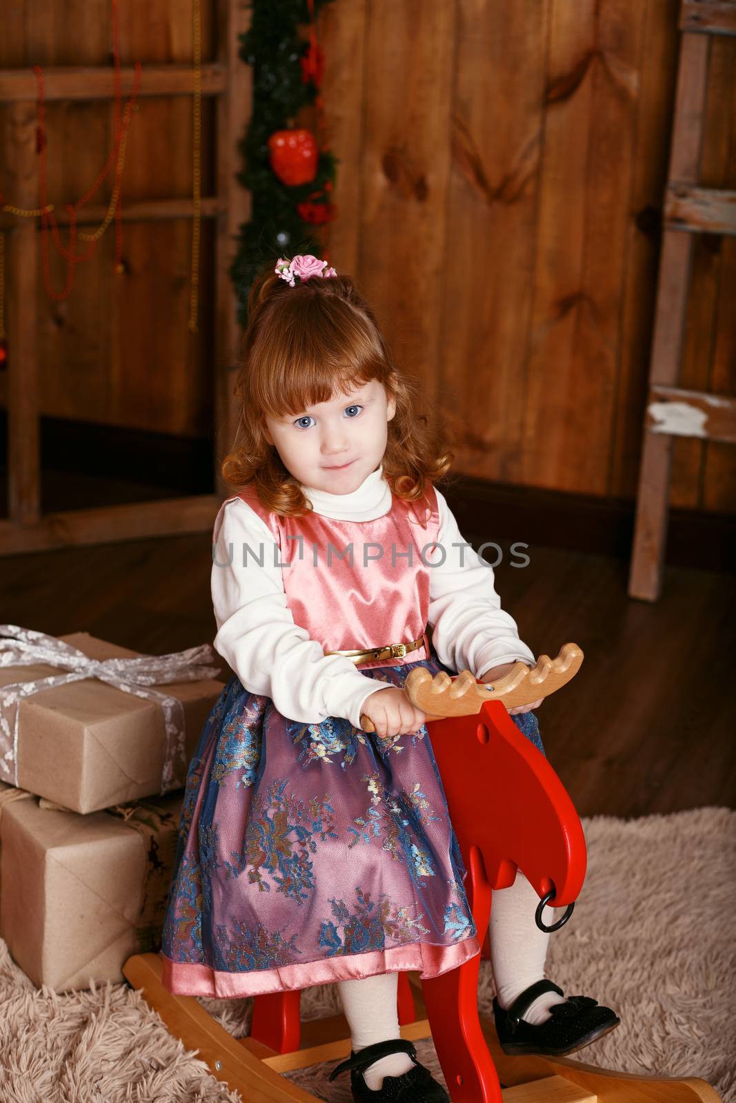 Portrait of a lovely little girl. Portrait of cute little girl among Christmas decorations. Girl riding a rocking deer. Rocking deer chair for kids ride playing